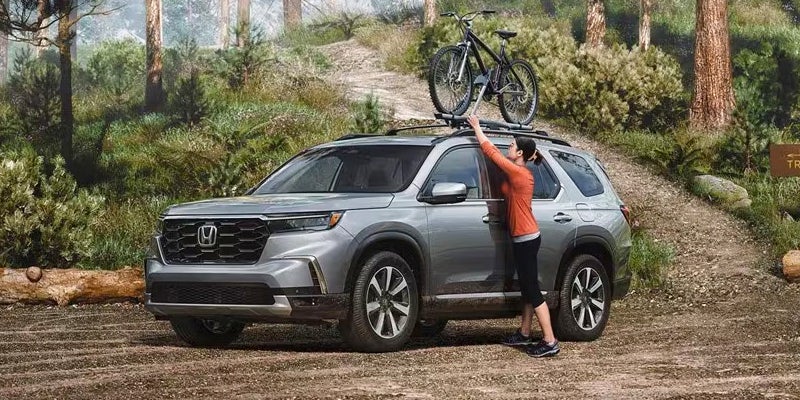A 2024 Honda Pilot and its owner is fixing his bike on top of the car.