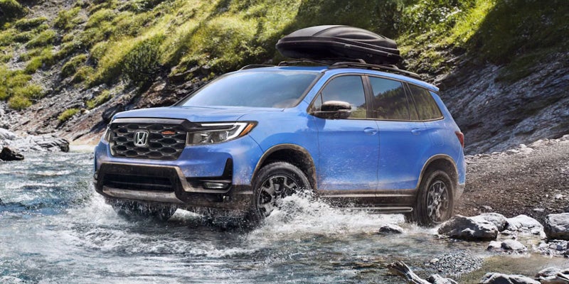 A light blue 2024 Honda Passport driving through shallow waters.