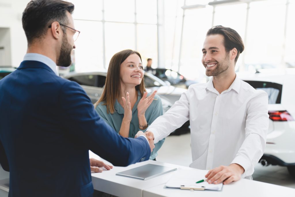 Financing at Honda of New Rochelle in New Rochelle, NY. A couple is settling the deal to purchase a new car. The husband is shaking the hand of the salesrep and the wife is clapping with a smile on her face.