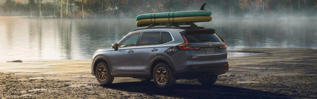 A Honda CR-V parked by a lake with kayaks on the roof.